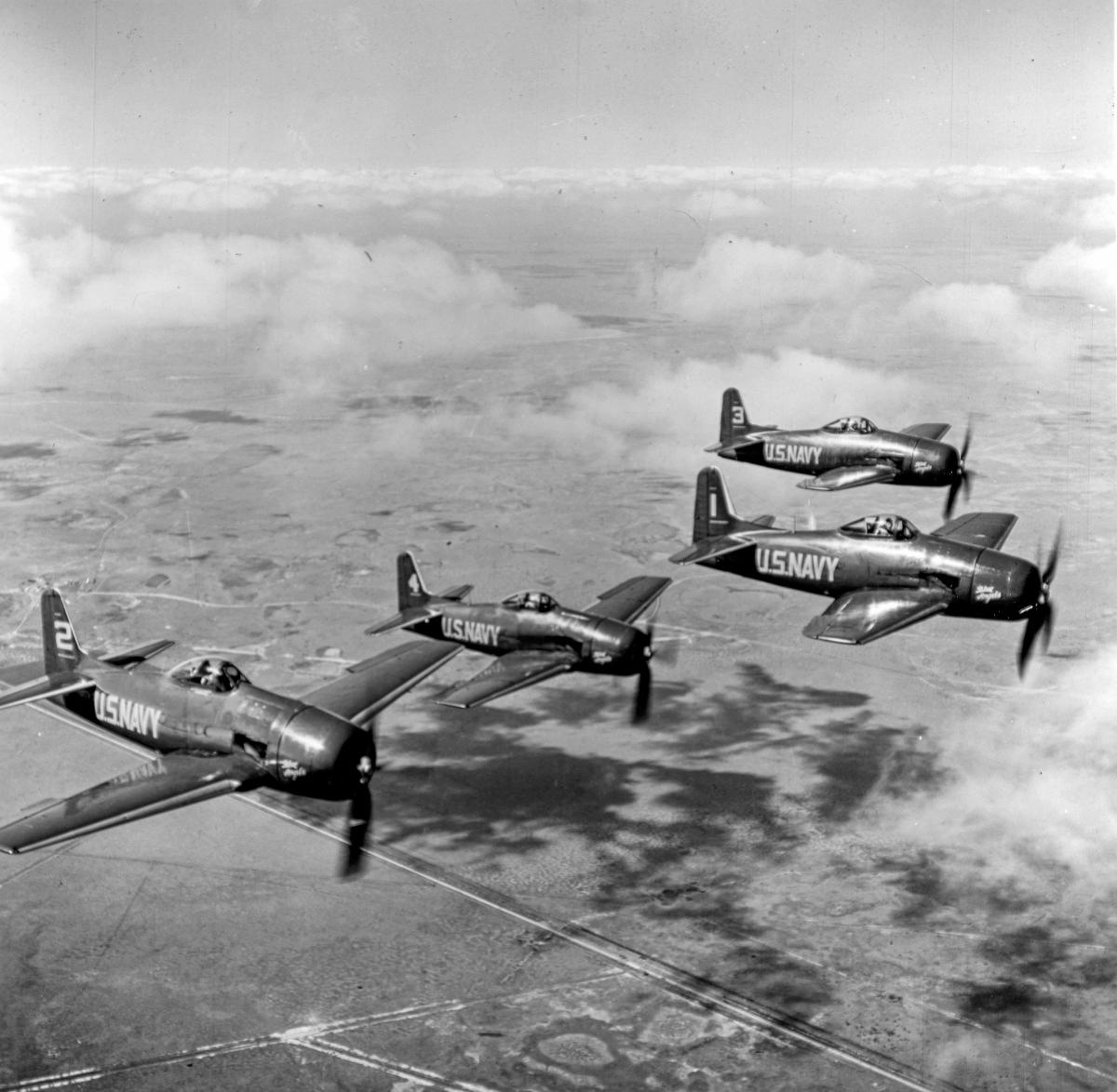 An aerial right side view of four Blue Angel F8F Bearcats flying in formation.