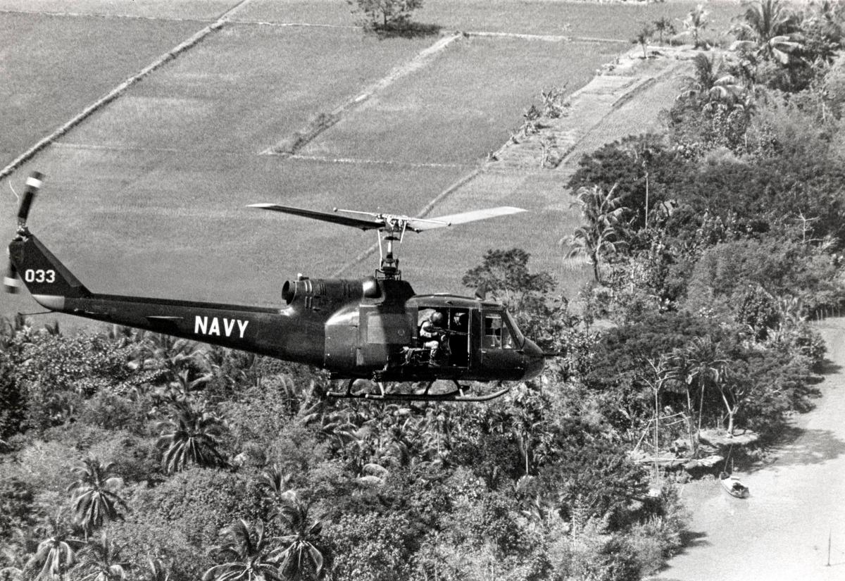 The right door gunner of a U.S. Navy Armed Gunship Helicopter (H-1 Iroquois) sits poised over the Mekong Delta, November 1967.