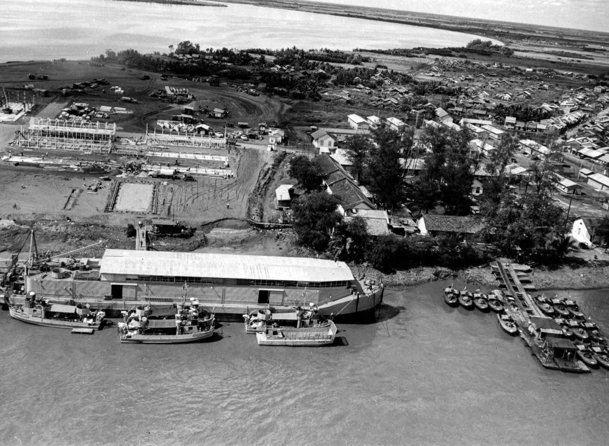 Nha Be (Naval Support Activity Base) is seen at left and Long Xuyen (U.S. Advanced Tactical Support Base) at right, while American PBR's can be seen in the water, Song Nha Be River, circa 1967.