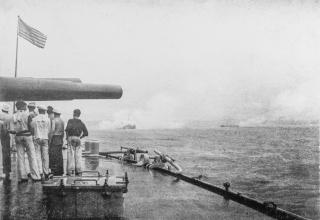 Iowa crewmen beneath the battleship’s forward 12-inch guns watch the Battle of Santiago. Smoke heavily shrouds the ship in the center.