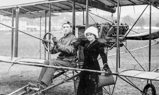  Eugene B. Ely seated in a Curtiss pusher biplane, with his wife, Mabel (Hall) Ely standing beside him