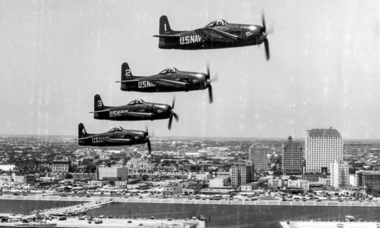 An aerial right side view of four F8F-1 Bearcat fighter aircraft in formation over Corpus Christi's water front area.