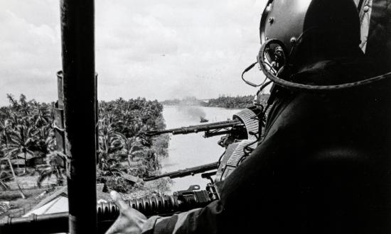 A door gunner of a U.S. Navy armed gunship helicopter (H-1 Iroquois) scours the riverbank for bad guys who ambushed a PBR (center), Mekong Delta, 9 November 1967