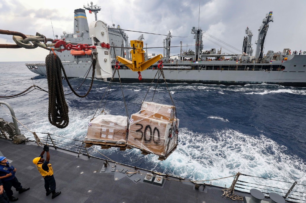 A man directs a crane carrying boxes onto a ship.