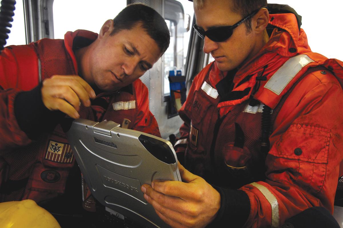 Coast Guardsmen view their position on a laptop computer while aboard a Coast Guard aids to navigation boat