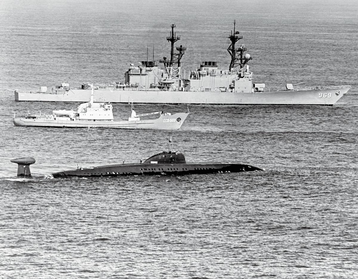 A starboard beam view of the destroyer USS Peterson (DD-969) underway near a Soviet Moma-class survey ship and a disabled Victor III class submarine