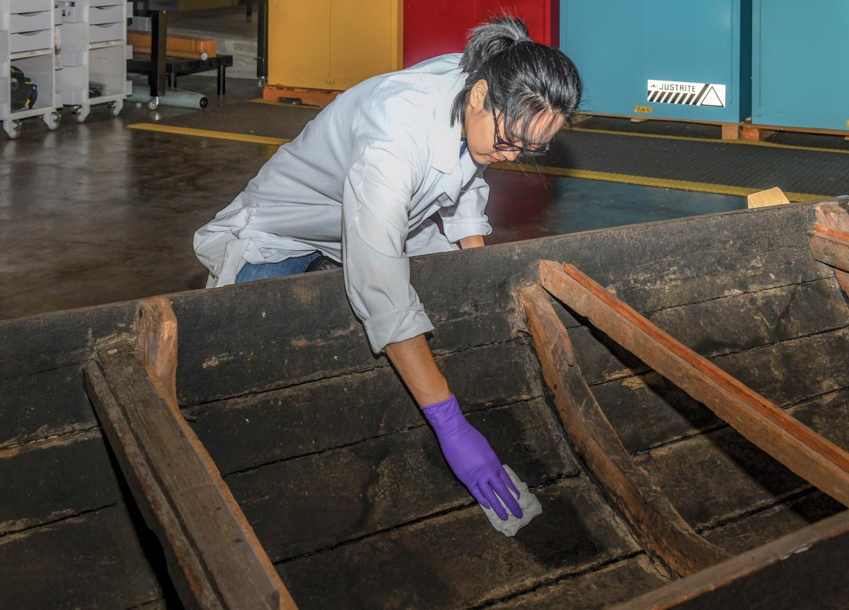 Conservator using distilled water to clean the planks of a Vietnamese sampan
