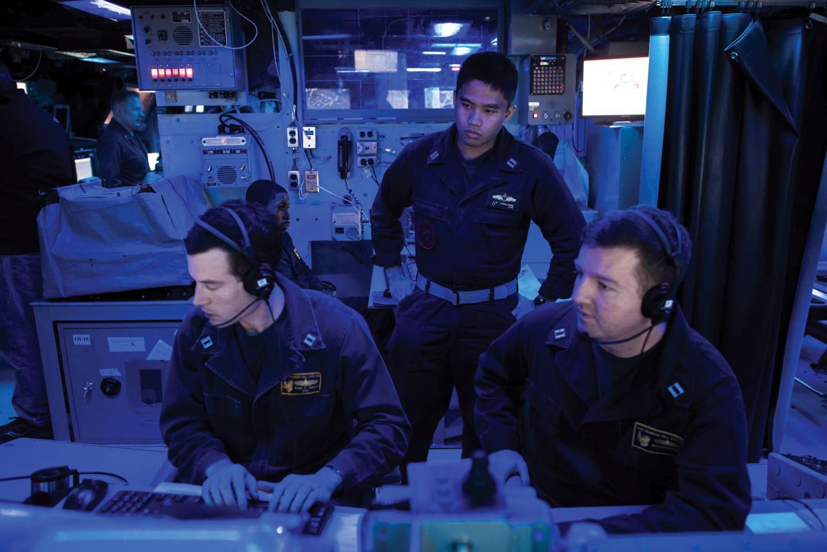 A surface warfare tactics instructor oversees the training of two officers on board the USS Bunker Hill (CG-52).