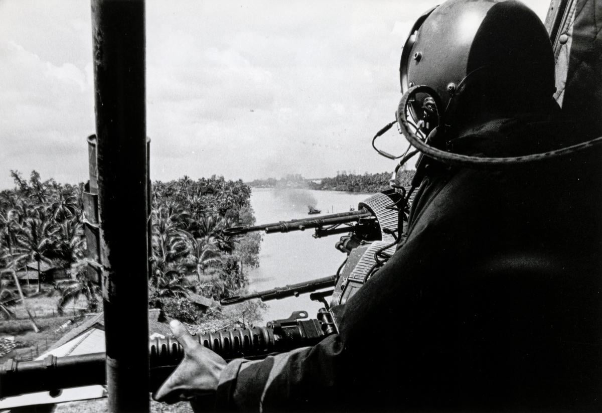 A door gunner of a U.S. Navy armed gunship helicopter (H-1 Iroquois) scours the riverbank for bad guys who ambushed a PBR (center), Mekong Delta, 9 November 1967