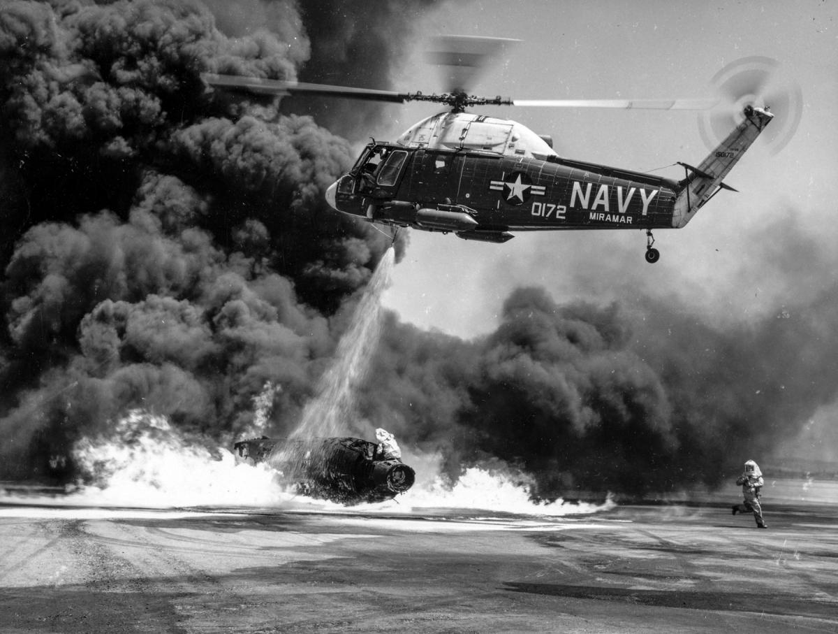 Helicopter spraying firefighting foam on an burning test aircraft