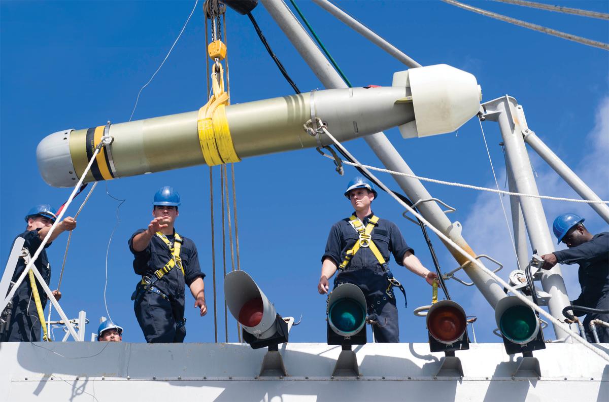 Sailors move a torpedo with a crane.