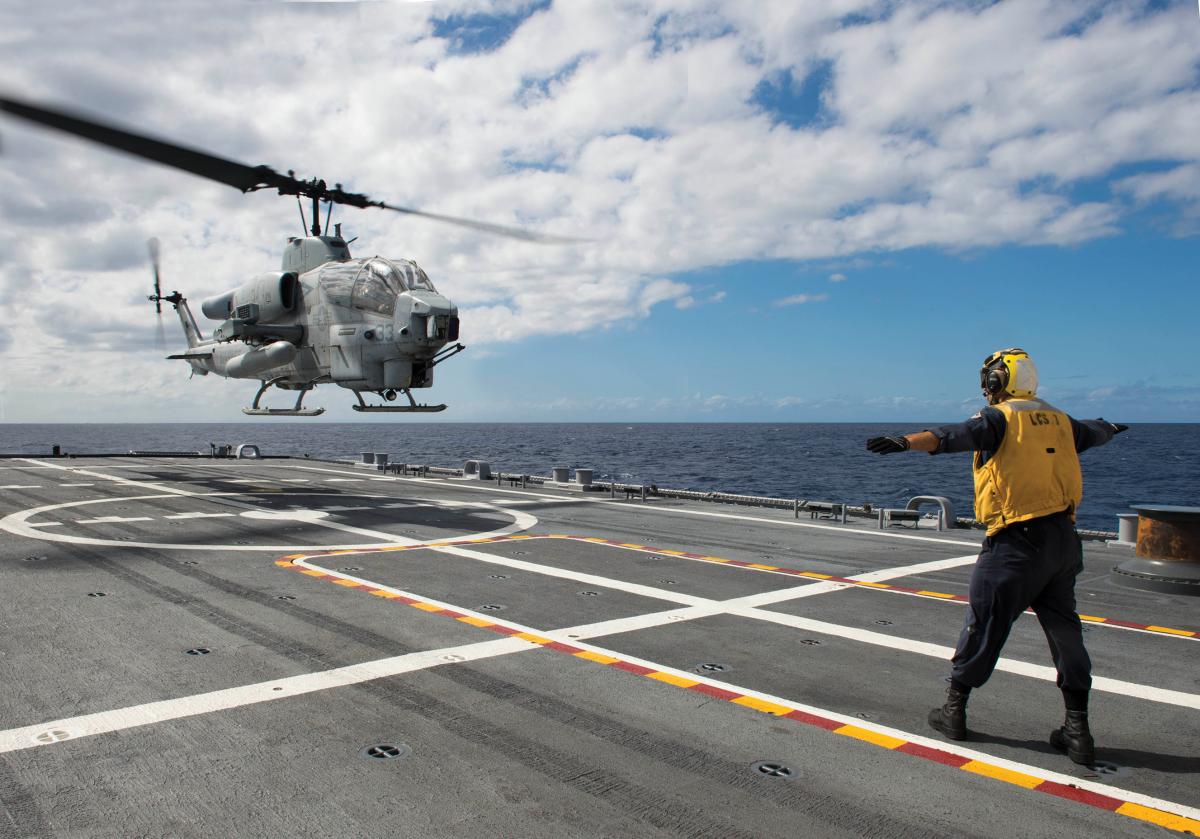 Sailor signals an AH-1 Cobra helicopter from Marine Air Group (MAG) 24 during deck landing qualification training aboard the littoral combat ship USS Fort Worth (LCS-3)