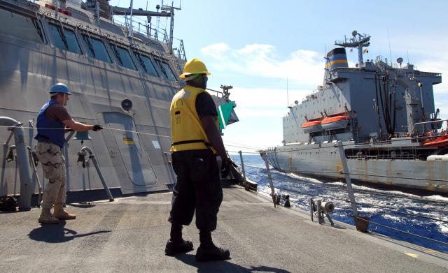 A chief logistics specialist on board the USS Freedom (LCS-1) signals the Military Sealift Command fleet replenishment oiler USNS Leroy Grumman (T-AO-195) during a refueling at sea. The Freedom-class LCS has an approximate displacement of 3,000 tons, compared with an oiler’s displacement of 40,000–80,000 tons, presenting special challenges in keeping the much smaller ship in proper position alongside.