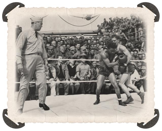 Retired professional boxer and Coast Guard Commander Jack Dempsey (left) gives an added punch when he referees a boxing match on the deck of a Coast Guard-manned troop transport headed for Europe during World War II.