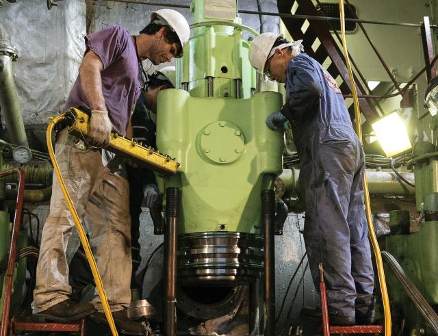 A chief engineer and port relief (shore gang) engineers lower an exhaust valve back into place atop the cylinder of a large two-stroke diesel engine on board the container ship M/V RJ Pfeiffer. Civilian chief engineers could perform similar hands-on work on board Coast Guard cutters, and train sailors and student engineers as well.