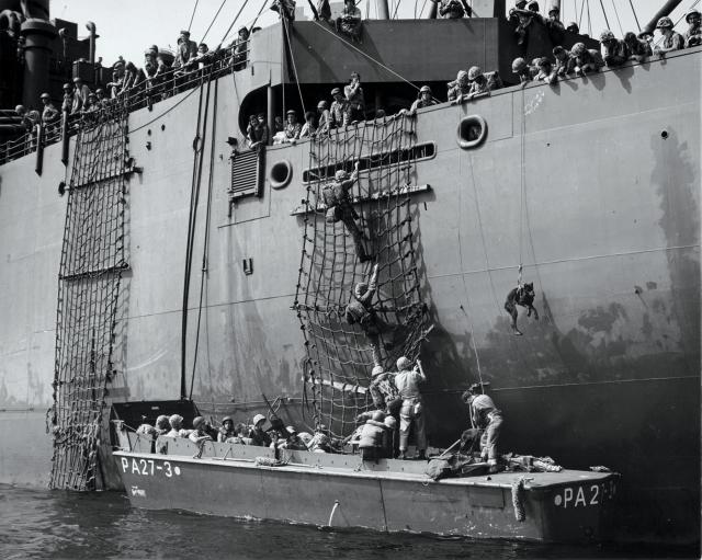 U.S. troops file down a landing net into a Higgins boat 