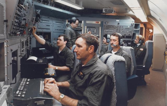 Navy submarine communications crew members man their stations in a mock-up of the E-6A TACAMO aircraft, developed to provide a communication link with ballistic-missile submarines.