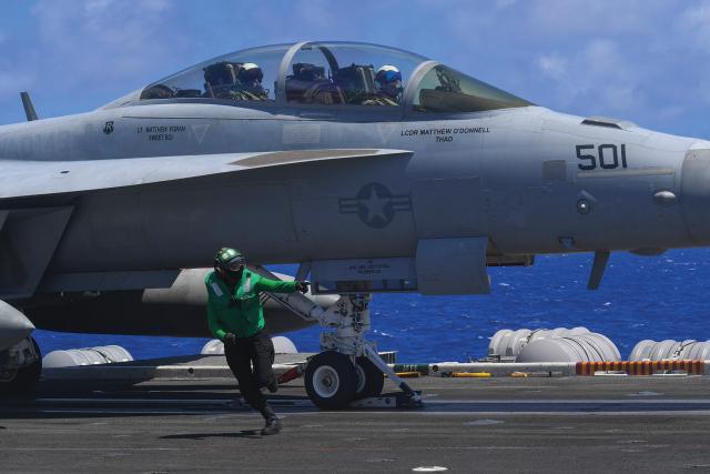 An aviation boatswain’s mate (equipment) runs across the USS Theodore Roosevelt (CVN-71) flight deck after connecting an E/A-18G Growler to the catapult. This duty is performed within inches of aircraft landing gear, beneath the aircraft nose. 