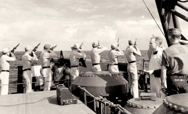 Following the Battle of Kula Gulf, Marines on board the USS Honolulu fire a salute during funeral services for a casualty from the sunken Helena.
