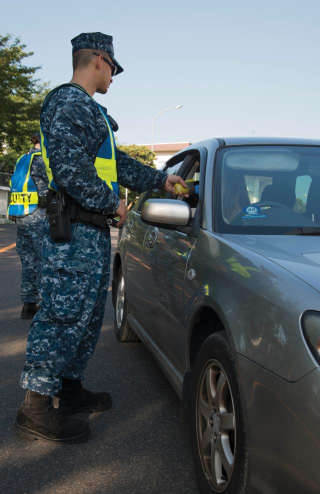 Sailor standing by an automobile administering a breathalyzer test to the driver