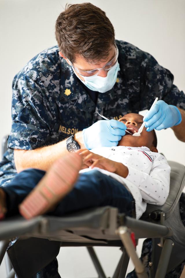 A dentist assigned to the hospital ship USNS Comfort (T-AH 20) operates on a young patient at one of two Enduring Promise 18