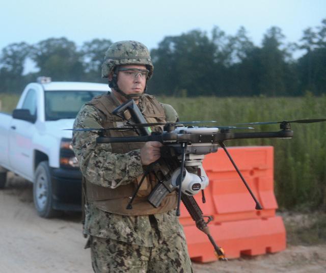 A Navy intelligence specialist assigned to Naval Mobile Construction Battalion One carries a SkyRaider R80D unmanned aerial system to a launch point during a field training exercise at Camp Shelby, Mississippi. More Navy IW personnel need to be trained for tactical, domestic homeland defense operations.