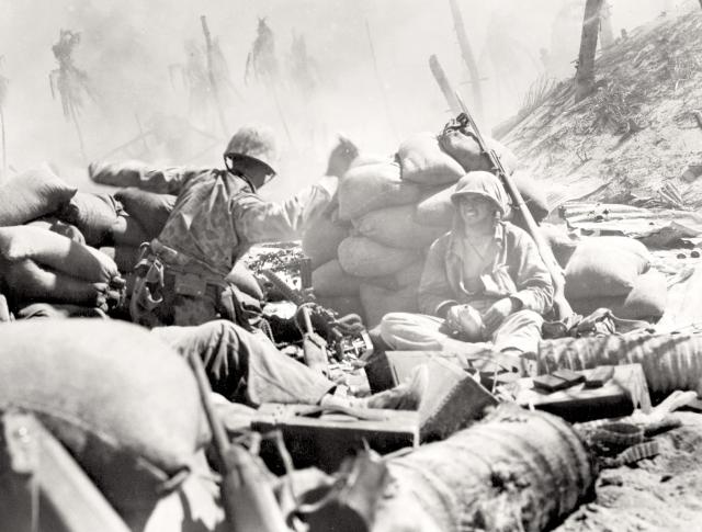 A Marine gets set to lob a hand grenade at a Japanese pillbox as the smoke of battle rolls over a hastily thrown-up sandbag entrenchment.