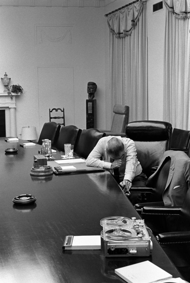 Lyndon Johnson leaning on a table while listening to a tape recorder