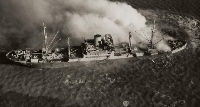 Smoke rises from the bow of a Japanese merchant ship, torpedoed in the South China Sea during World War II. During that conflict, U.S. Navy submarines and planes regularly targeted Japanese shipping in the Pacific.