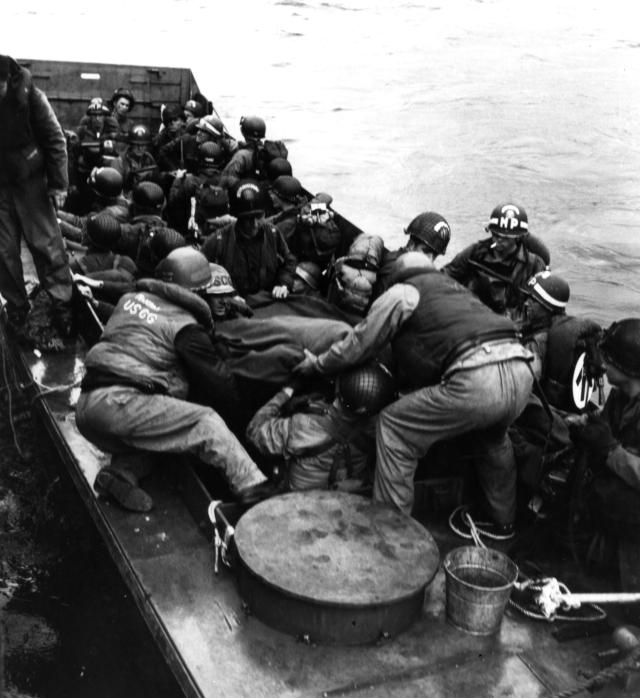 Coast Guard coxswain hit by German machine-gun fire is moved from his landing craft to a transport for treatment on D-Day