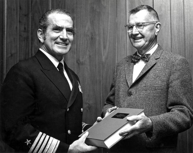 Admiral Zumwalt handing Rear Admiral George Bauernschmidt a bound copy of his oral history.