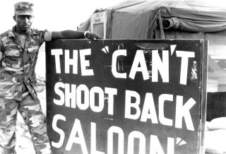 July 1983: A Marine stands alongside a mordant sign that captures feelings prevalent among the multinational force—feelings about restrictive rules of engagement in increasingly hostile environs.