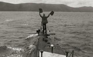 A Navy sailor uses flag semaphore to signal the coast from the deck of his submarine.