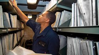 A sailor on board the aircraft carrier USS Harry S. Truman (CVN-75) sorts through technical documents. Before it can execute any mission, a warship crew must first safely navigate the ship, land and launch aircraft, and operate a complex industrial plant. Millions of minuscule management tasks that deliver a fully ready warship are brought to bear in minutes or seconds of danger and uncertainty.