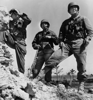 On a rocky-ledge observation post, Major General Lemuel C. Shepherd, Commanding General, 6th Marine Division (center), is flanked by his assistant commander, Brigadier General William T. Clement (right), and  Commanding General of the Tenth Army, Lieutenant General Simon Bolivar Buckner (left).