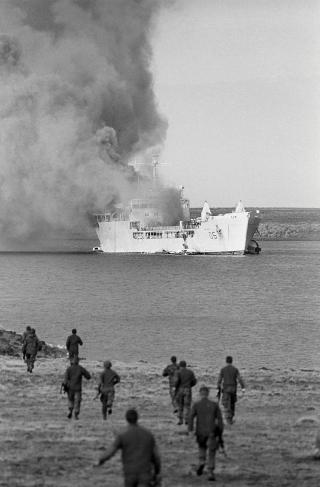 British personnel rush toward the shore of Bluff Cove soon after the landing ship Sir Galahad, loaded with Welsh Guardsmen, was hit by 500-pound bombs