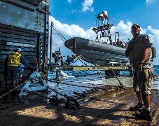 A civilian mariner assigned to Military Sealift Command prepares to launch a rigid-hull inflatable boat from a Navy ship during mine countermeasures exercises. The United States has long made common use of hybrid crews, combining civilian mariners with Navy service members, opening the door to considering PAFMM boats military auxiliaries. 