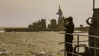 A sailor stands port lifebuoy watch on the fantail of the USS Abraham Lincoln (CVN-72) as the Japan Maritime Self-Defense Force guided-missile destroyer Kongō sails in formation.