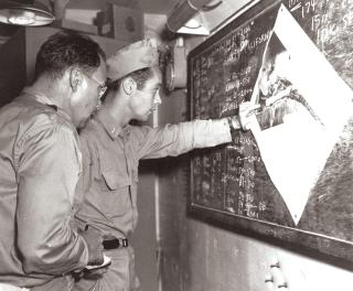 A war correspondent and an ensign of Torpedo Squadron 16 (VT-16) examine an aerial photograph of Tarawa Atoll’s Betio Island in a ready room on board the USS Lexington, 17 September 1943. The carrier’s planes would raid the island the following day.