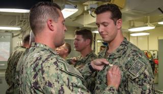 A surface warfare officer is pinned on board the USS Gerald R. Ford (CVN-78). Platform or billet specialization should occur after the first division officer tour, allowing SWOs to hone their skills and become true experts before received their SWO pin. 