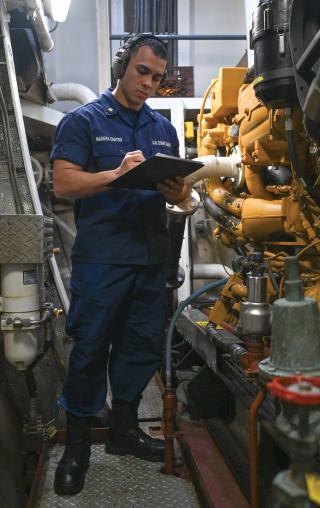 A machinery technician on board the USCGC Seneca (WMEC-906) conducts an in-port maintenance round in the cutter’s engine room in May 2024. Even with improved data collection from the MCS, every cutter still has a watchstander walking around with a clipboard and pen to check equipment that does not interface well with the system.