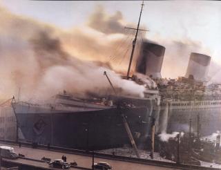The SS Normandie catches fire and sinks at Pier 88 in Manhattan, 9 February 1942. While it would turn out that a welding-torch spark did her in, that spark also would further ignite the paranoia of a public already fearful of pro-German spies operating in the region.