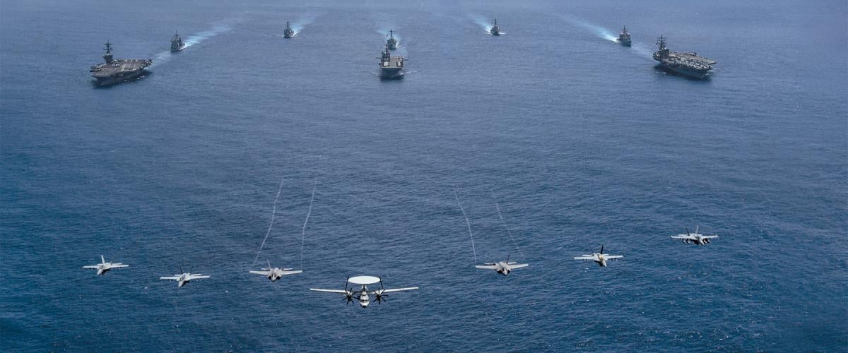 Aircraft from Carrier Air Wing 9 fly over the aircraft carrier USS Abraham Lincoln (CVN-72, front left), Tripoli (LHA-7, front center), Ronald Reagan (CVN-76, front right), Mobile Bay (CG-53, middle left), Benfold (DDG-65, middle center), Antietam (CG-54, middle right), Spruance (DDG-111, back left), and Fitzgerald  (DDG-62, back right) as they sail in formation in the Philippine Sea during Valiant Shield 2022.