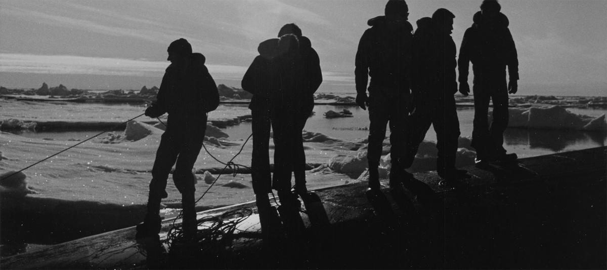 Crewmen of the nuclear-powered attack submarine  USS Queenfish (SSN-651) hold a safety line for scuba divers in a rubber raft near the North Pole. The divers are preparing to observe and photograph the underside of the ice.