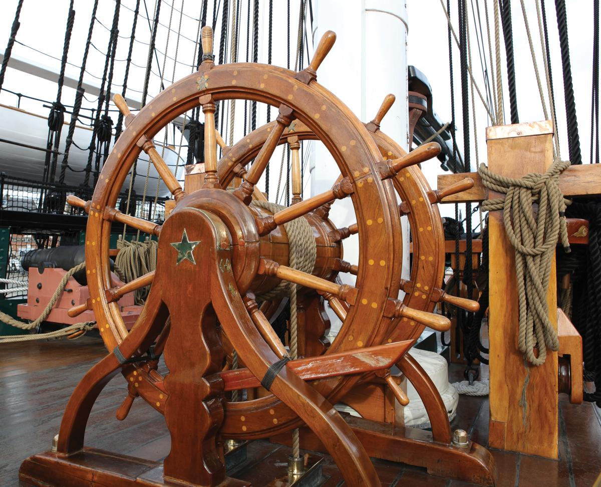 The helm of the USS Constitution shows the characteristic features of ships’ wheels from the time before steam or electric motors controlled the rudder. Two wheels, separated by a winch barrel, allowed extra helmsmen to assist in heavy weather. The barrel is connected through the deck by a series of blocks and tackles to the tiller, which turns the rudder.