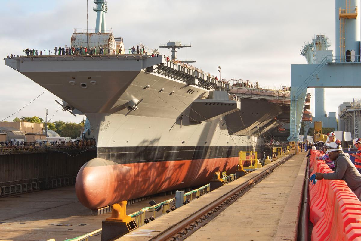 The aircraft carrier John F. Kennedy (CVN-79)—shown in dry dock prior to her christening and 17 December launch—is scheduled to deliver to the Navy in 2022.