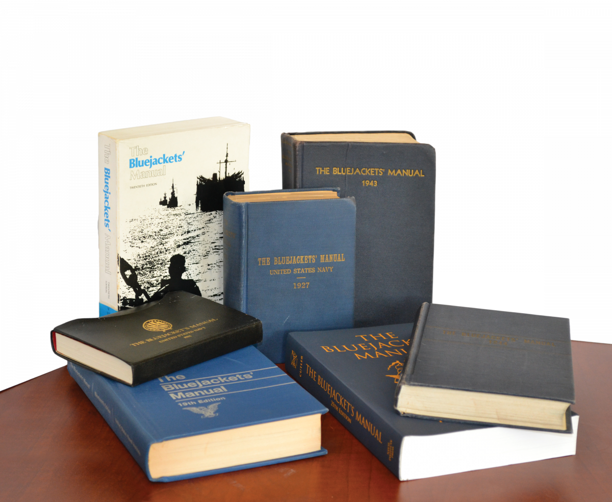 Seven different editions of the Bluejacket's Manual on a table