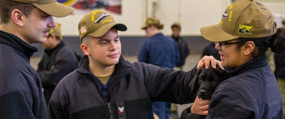 Sailors play with a dog from Mutts with a Mission on board the USS Gerald R. Ford (CVN-76) as part of a morale boosting event. Science has shown dogs can help fight stress—one of many options the Navy should consider.  