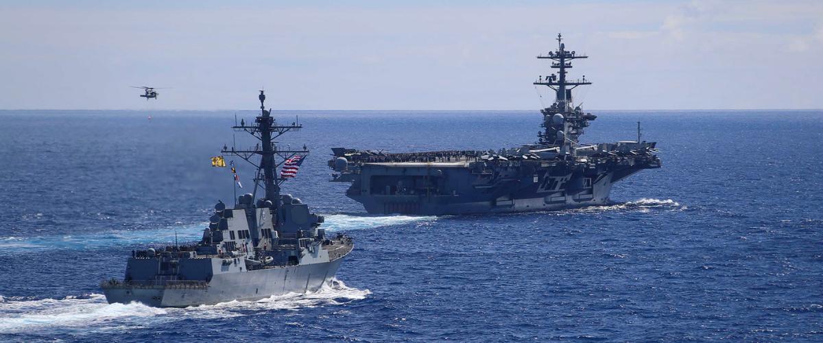The Arleigh Burke-class guided missile destroyer USS Spruance (DDG 111) sails alongside the Nimitz-class aircraft carrier USS Abraham Lincoln (CVN 72) as an MH-60S Sea Hawk helicopter, assigned to the “Chargers” of Helicopter Sea Combat Squadron (HSC) 14, flies by during an air power demonstration for embarked guests. 