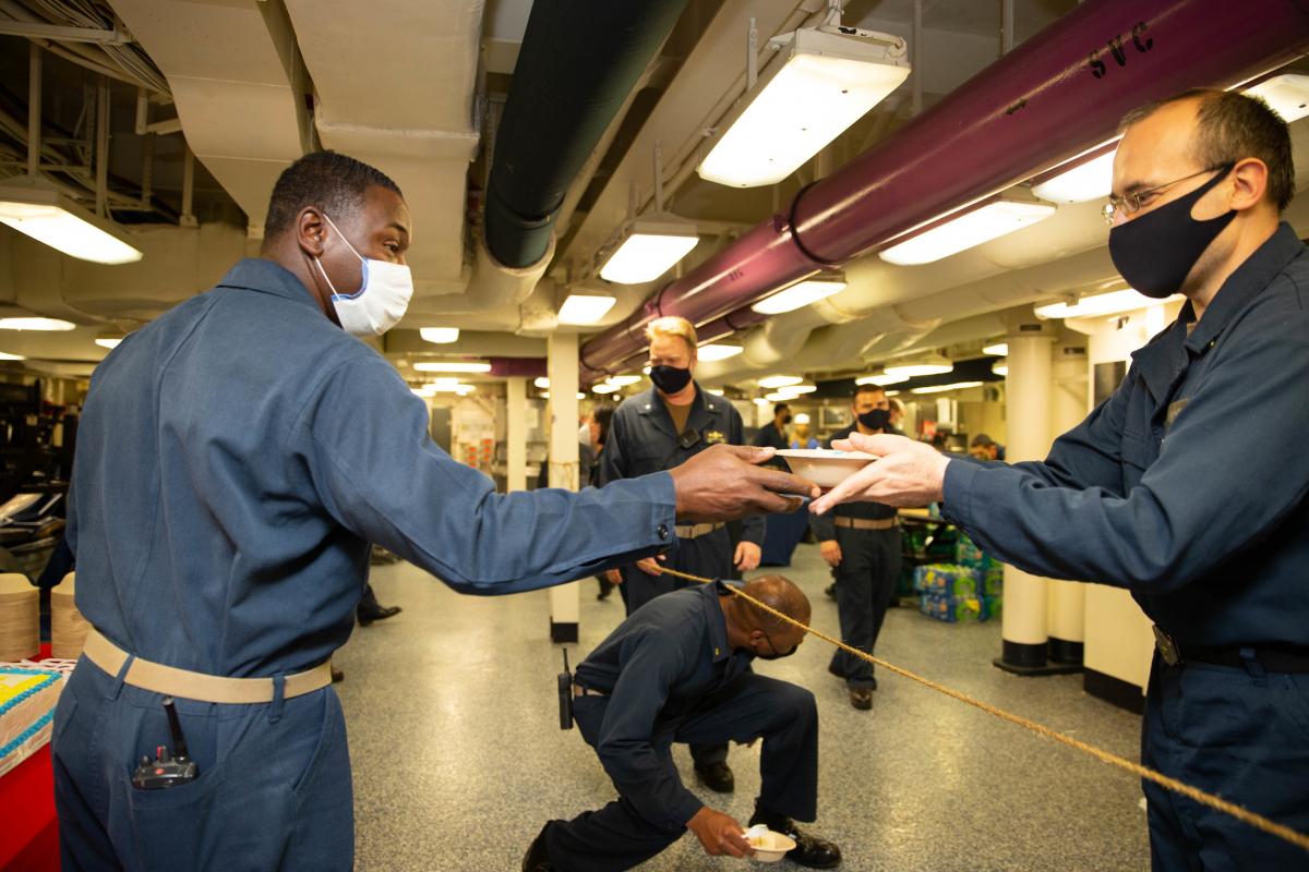 The USS Gerald R. Ford (CVN-78) command master chief hands out cake to sailors to commemorate the ship’s three-year commissioning anniversary. The Ford’s sailors are executing battle messing in spaces that accommodate six-foot social distancing.  